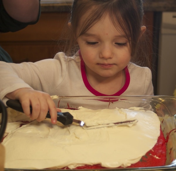 4 year old girl frosting a cake.