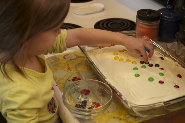 Little girl decorating a cake with M&Ms. 