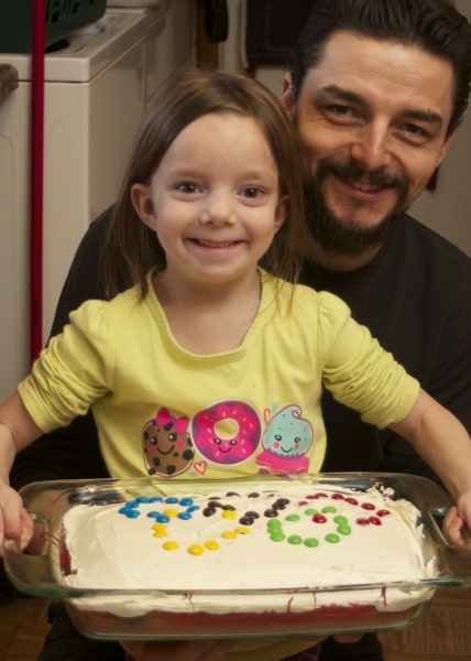Father and daughter posing with the Olympic rings cake they baked together. 