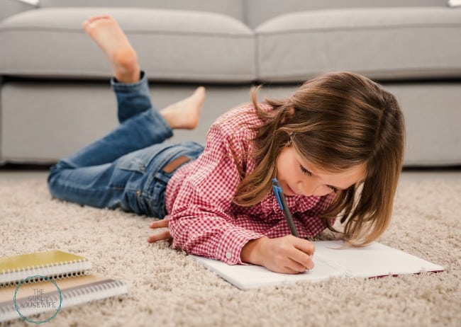 Little girl laying on floor doing her homeschool schoolwork. 