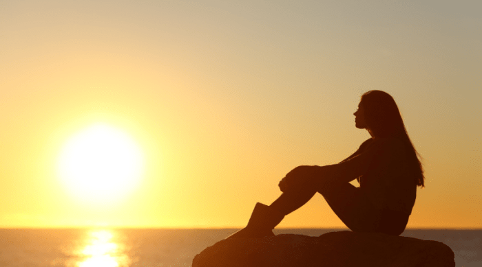 Woman silhouette watching sun in a sunset