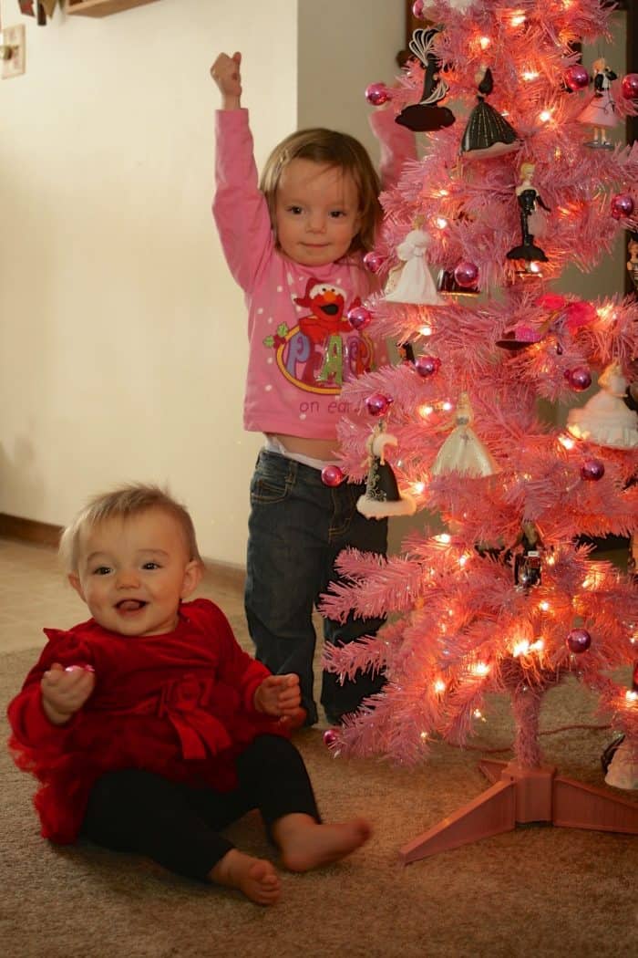 2 young sisters around a pink Christmas tree