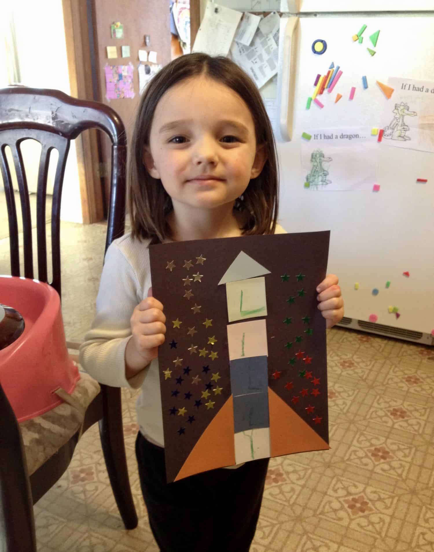 Little girl holding up her rocket craft with her name on it